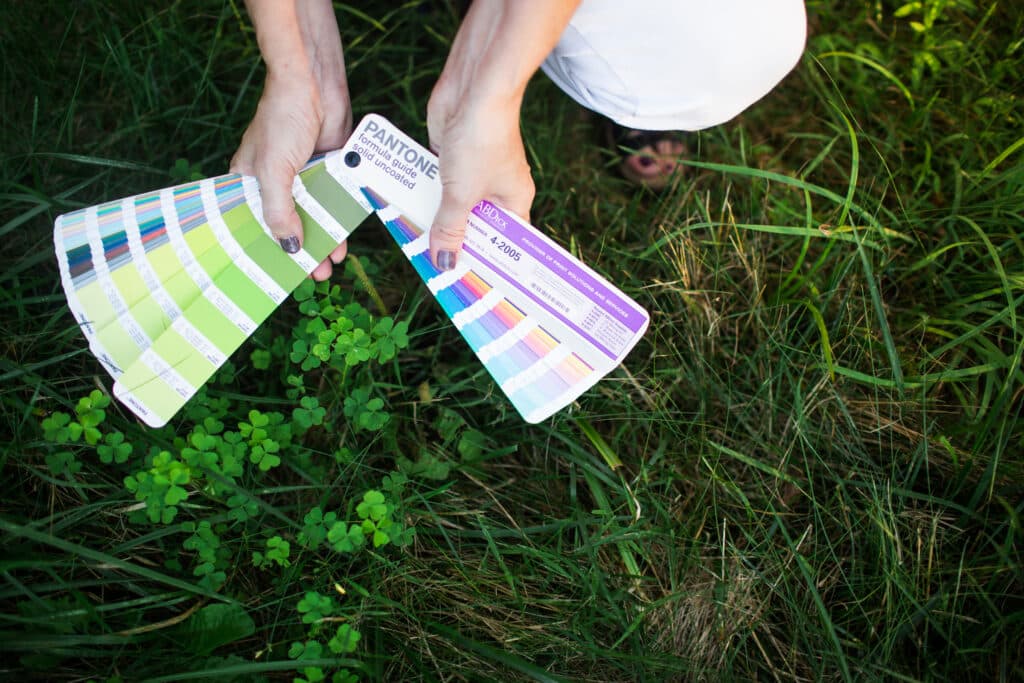 Two hands holding a Pantone swatch book over grass and clover